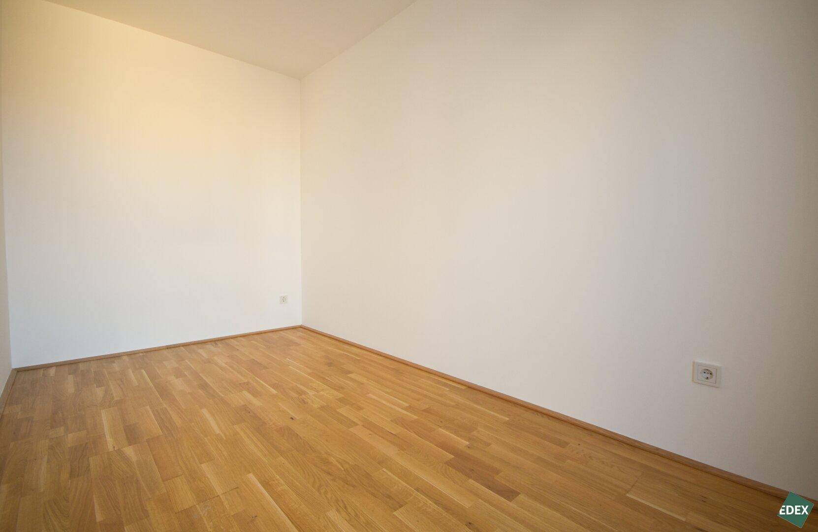 Helles, leeres Zimmer mit Holzboden, ideal als Schlaf- oder Arbeitszimmer.