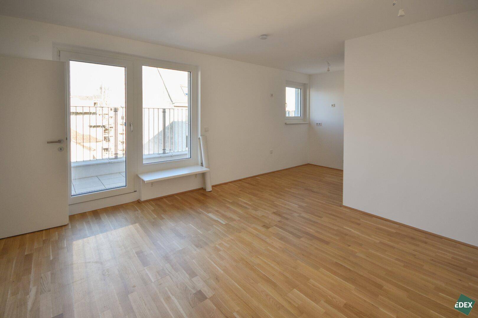 Lichtdurchfluteter Wohnraum mit Holzboden und direktem Zugang zu einem Balkon.