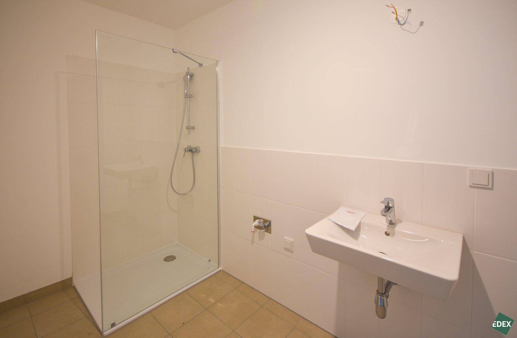 Modernes Badezimmer mit Duschkabine, Waschbecken und hellen Fliesen an den Wänden.
