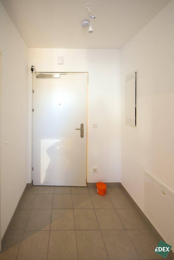 Heller Eingangsbereich mit Fliesenboden und weißer Eingangstür in einem modernen Gebäude.