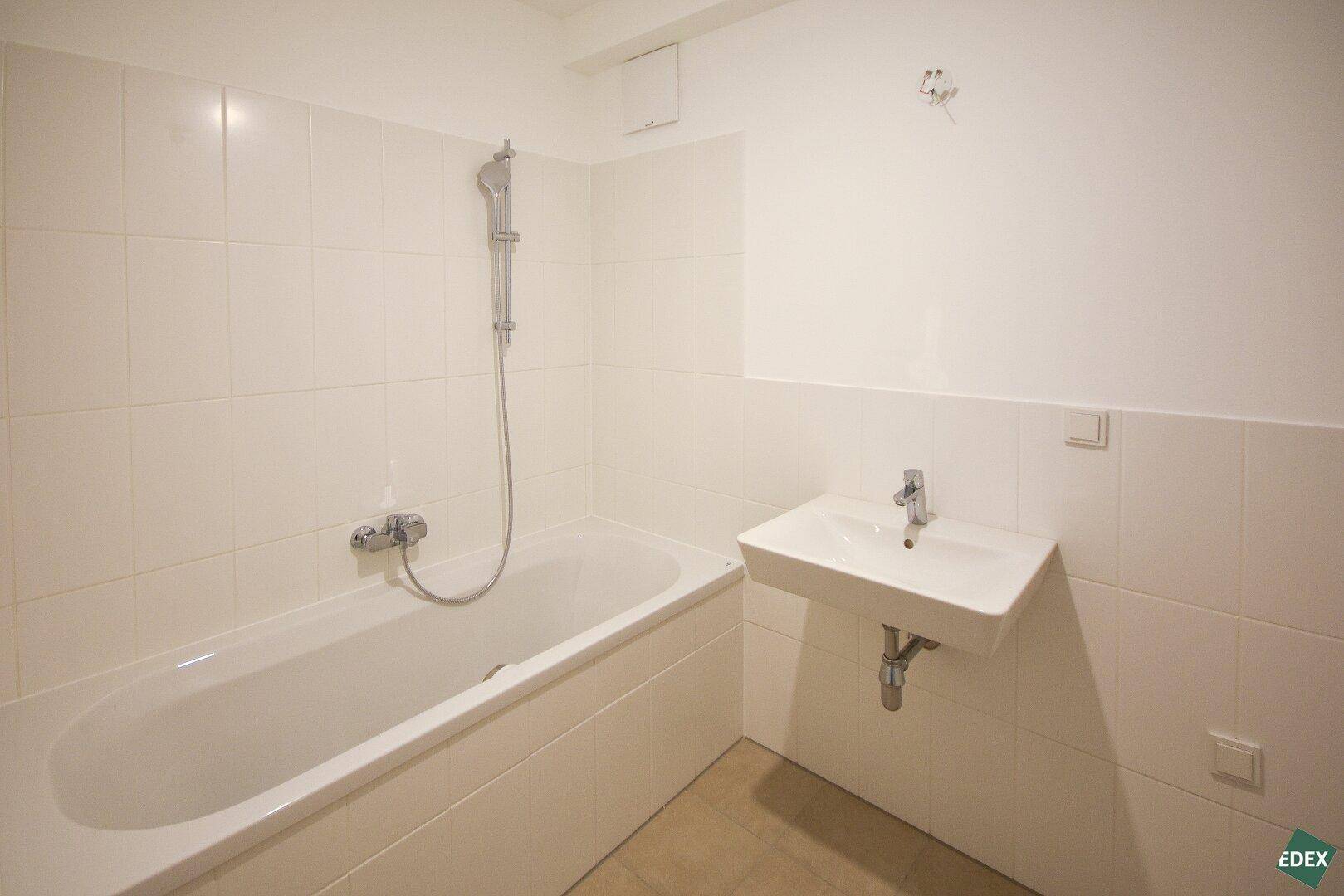 Modernes Badezimmer mit Badewanne, Waschbecken und weißen Fliesen, funktional und hell.
