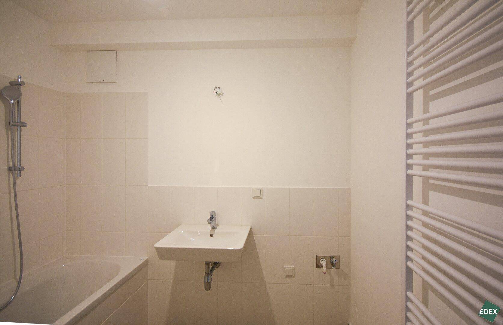 Helles Badezimmer mit Badewanne, Waschbecken und beheiztem Handtuchhalter, praktisch eingerichtet.
