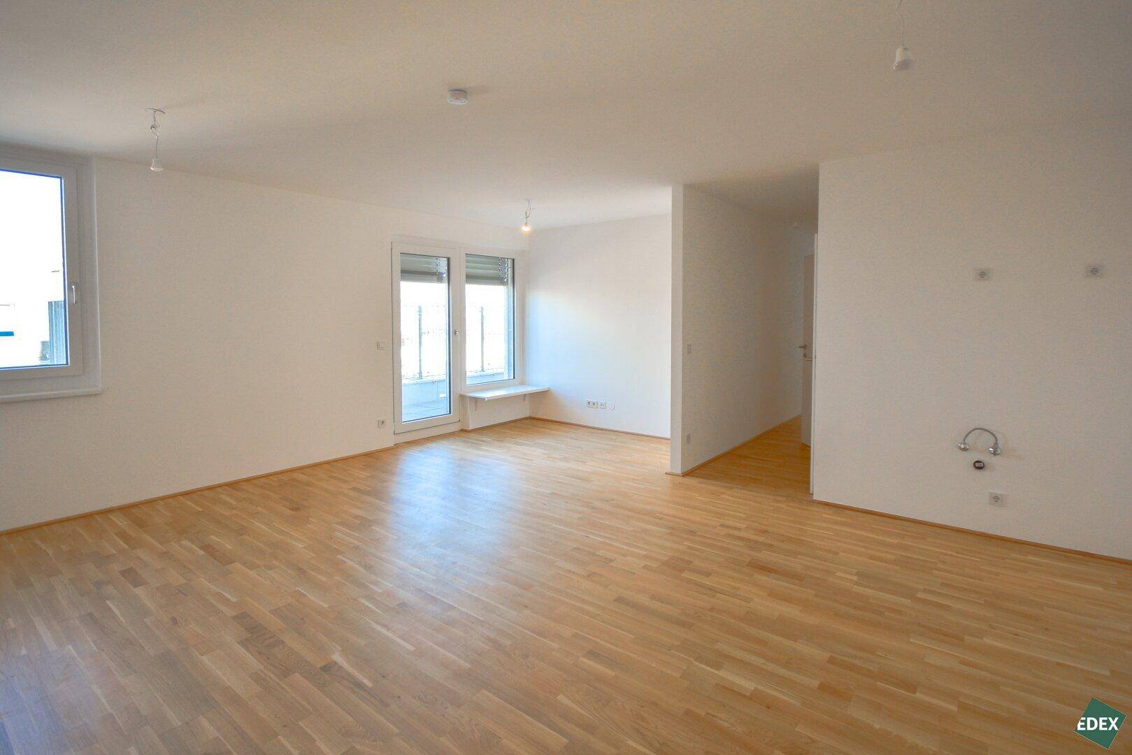 Geräumiges, leeres Wohnzimmer mit Holzboden und großen Fenstern für viel Tageslicht.