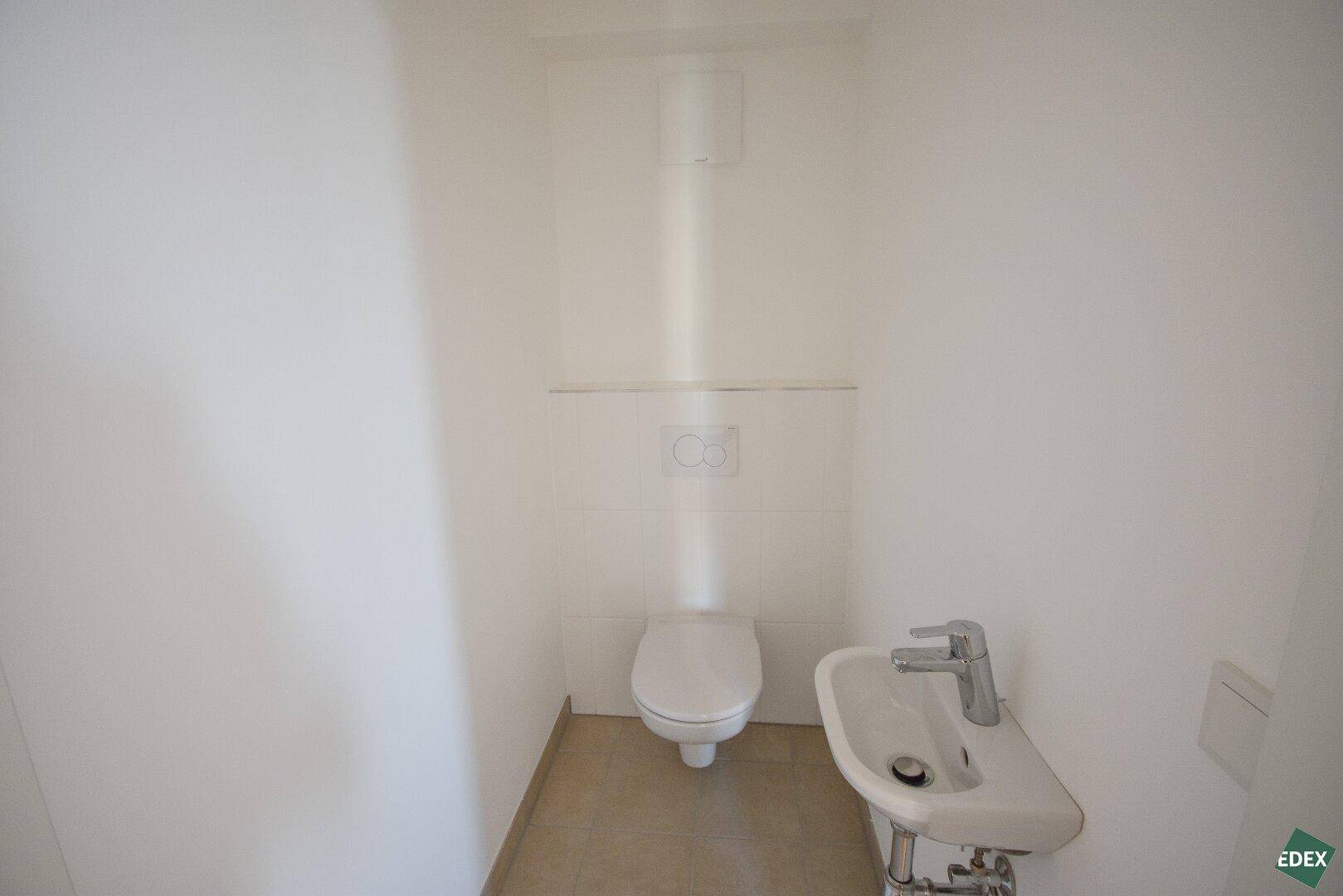 Separates WC mit wandhängender Toilette und kleinem Waschbecken, sauber und funktional.