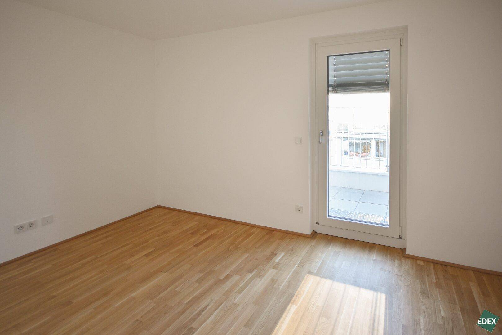 Helles Schlafzimmer mit Holzboden und Zugang zu einem Balkon, ideal für frische Luft.