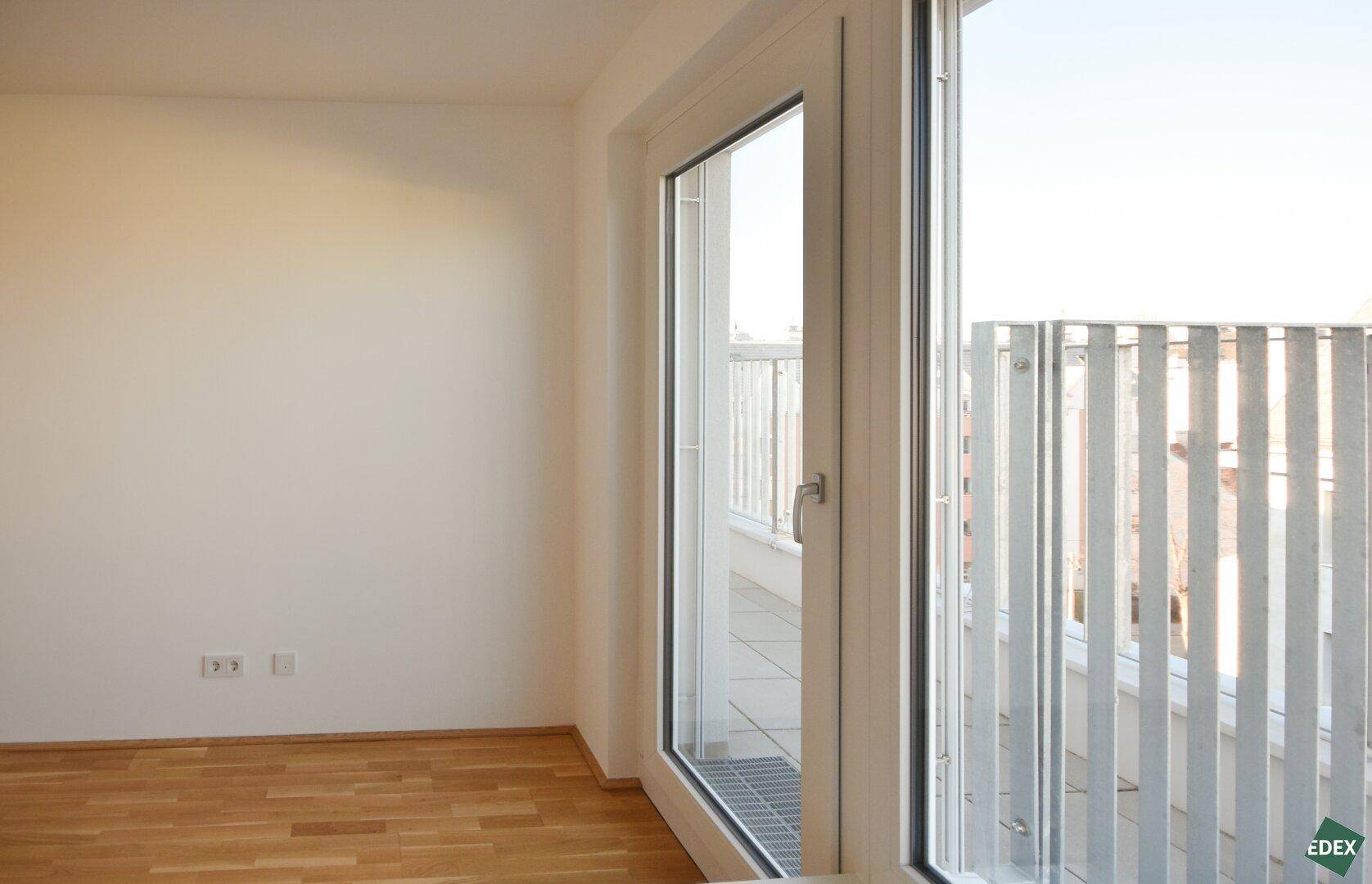 Detailansicht des Balkonzugangs in einem hellen Schlafzimmer mit Holzboden.