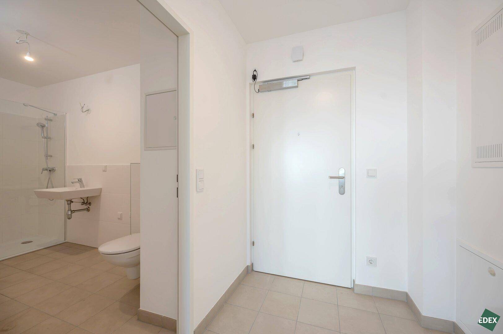 Eingangsbereich mit Fliesenboden und Blick in ein modernes Badezimmer mit Dusche und WC.