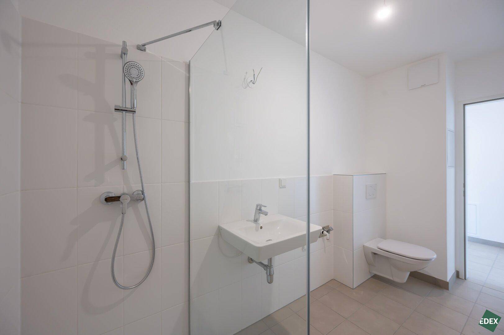 Helles Badezimmer mit moderner Dusche, Waschbecken und Wand-WC, ausgestattet mit Fliesenboden.