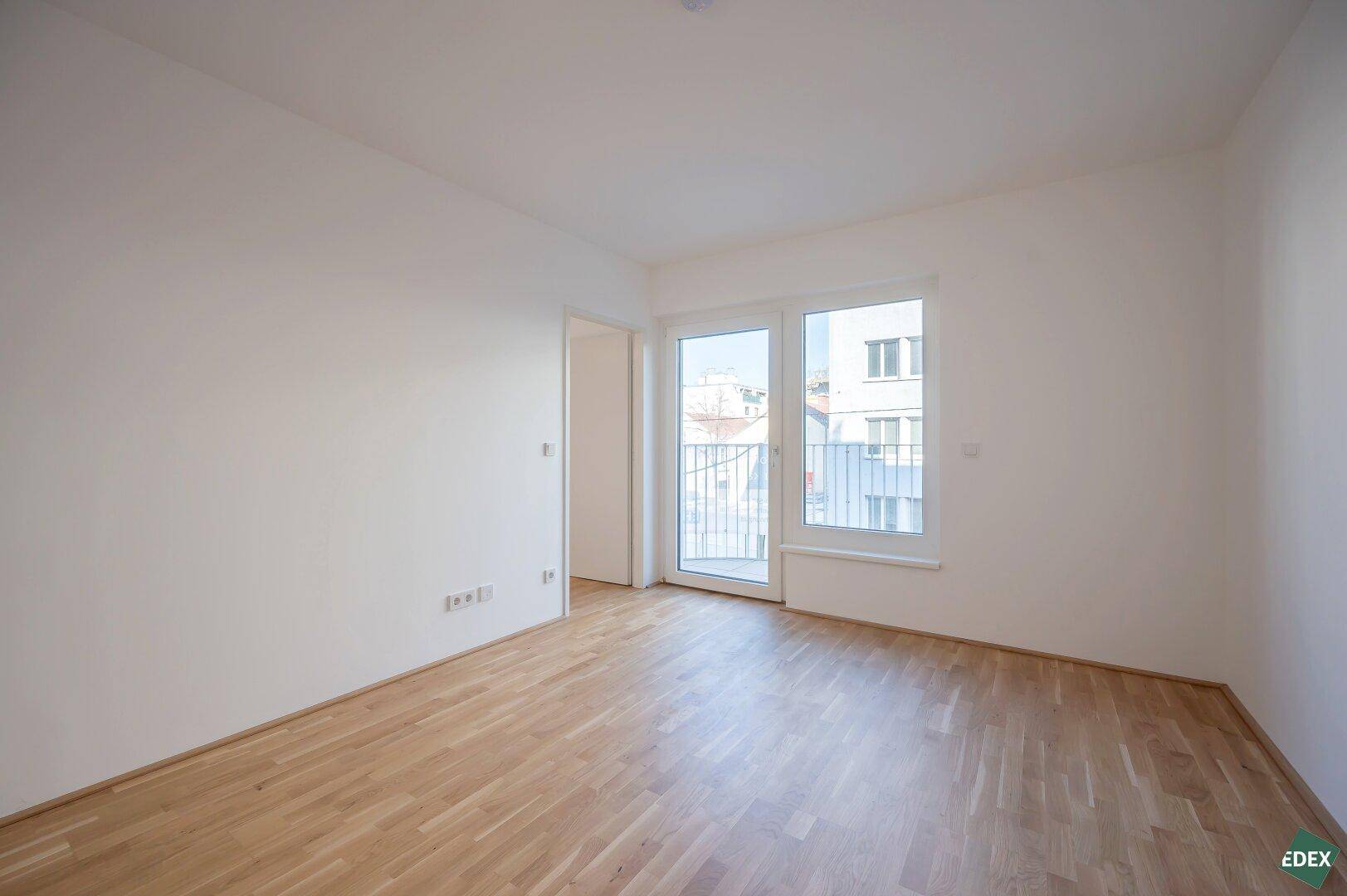 Helles Zimmer mit Parkettboden und Zugang zu einem französischen Balkon, ideal als Schlafzimmer.