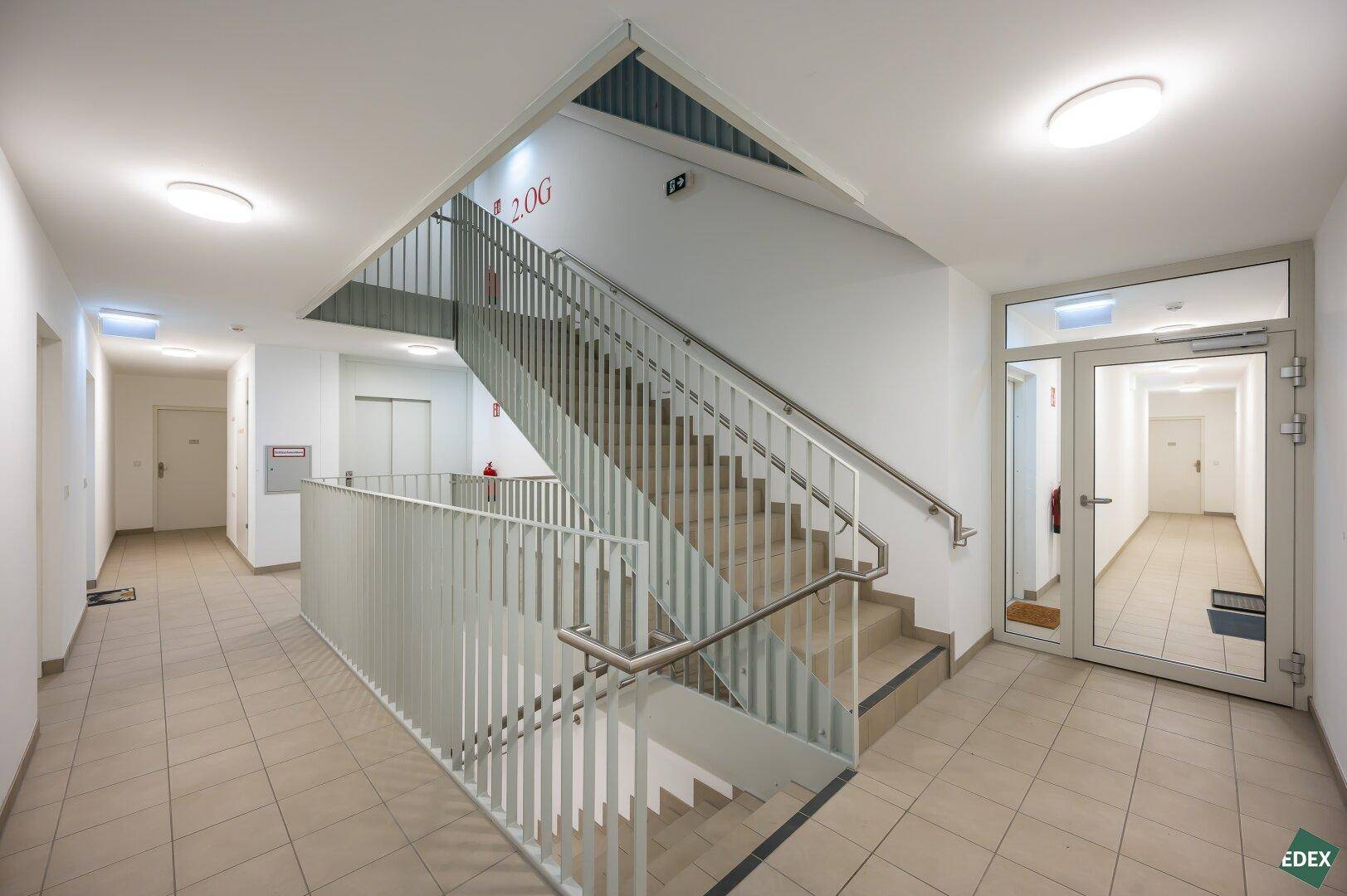 Heller Treppenaufgang in einem modernen Mehrfamilienhaus mit Fliesenboden und Metallgeländer.