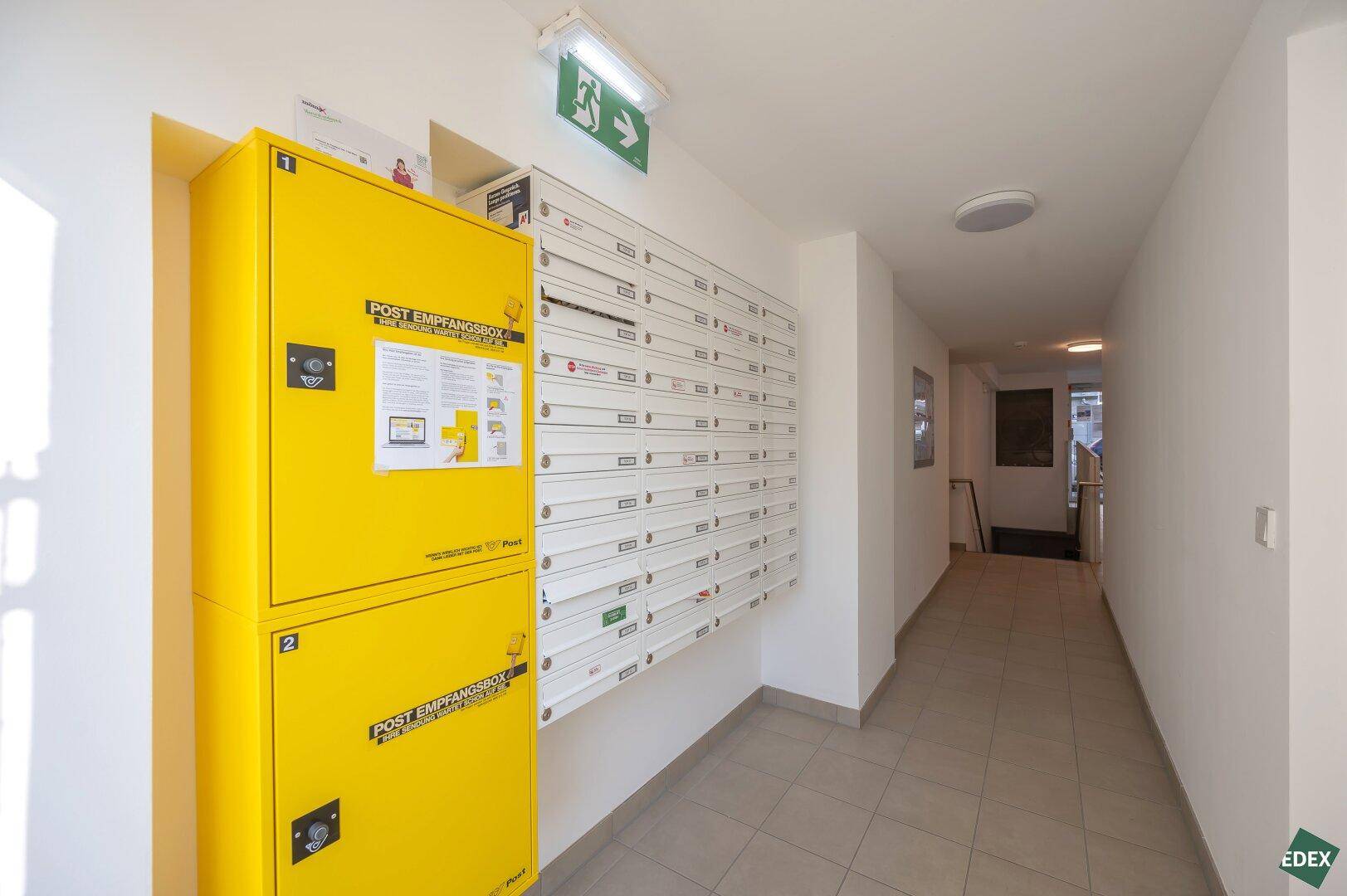Eingangsbereich mit gelben Paketboxen und zahlreichen Briefkästen, modern und funktional.