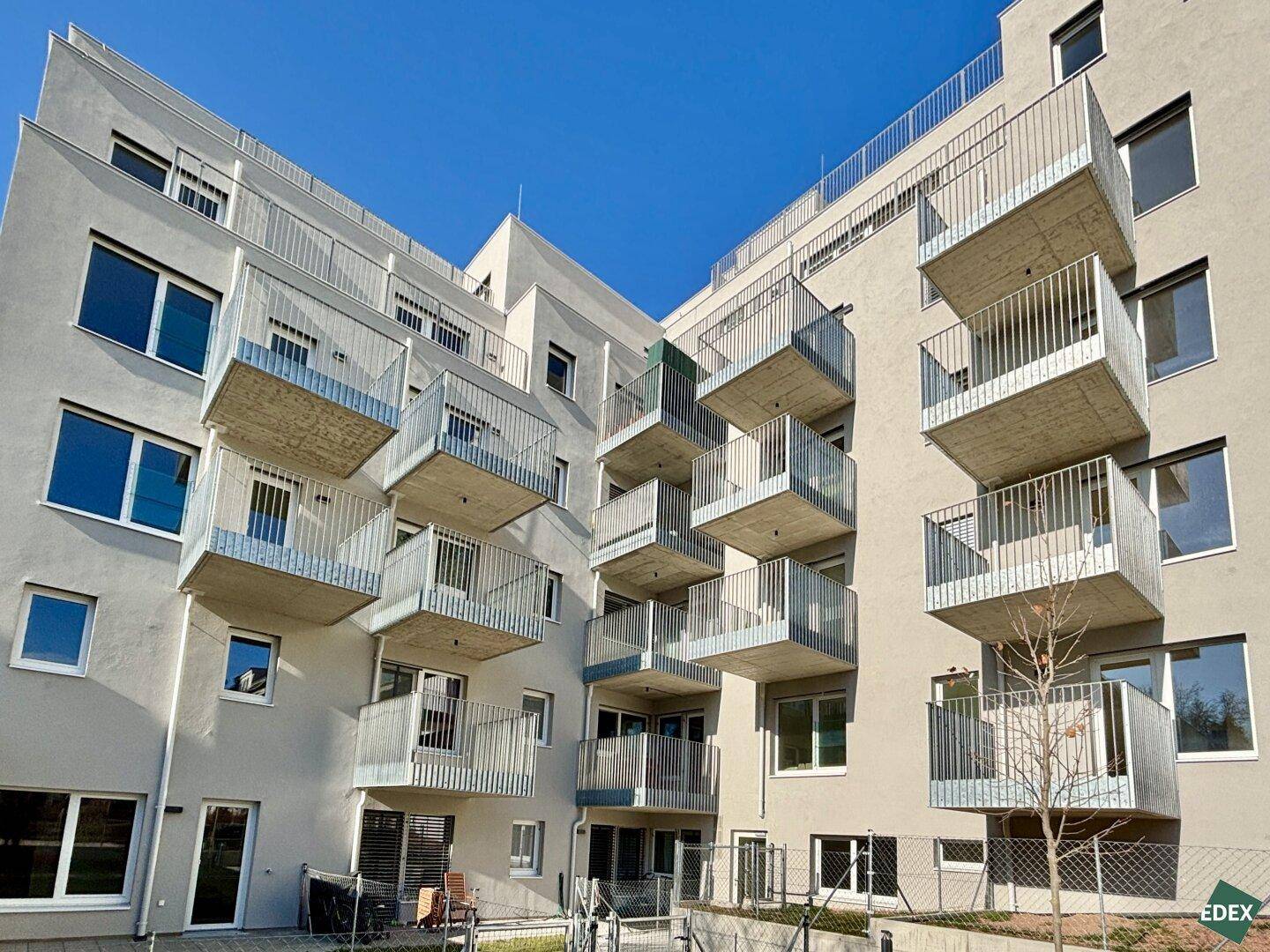 Moderne Wohnanlage mit zahlreichen Balkonen und gepflegten Außenbereichen unter blauem Himmel.