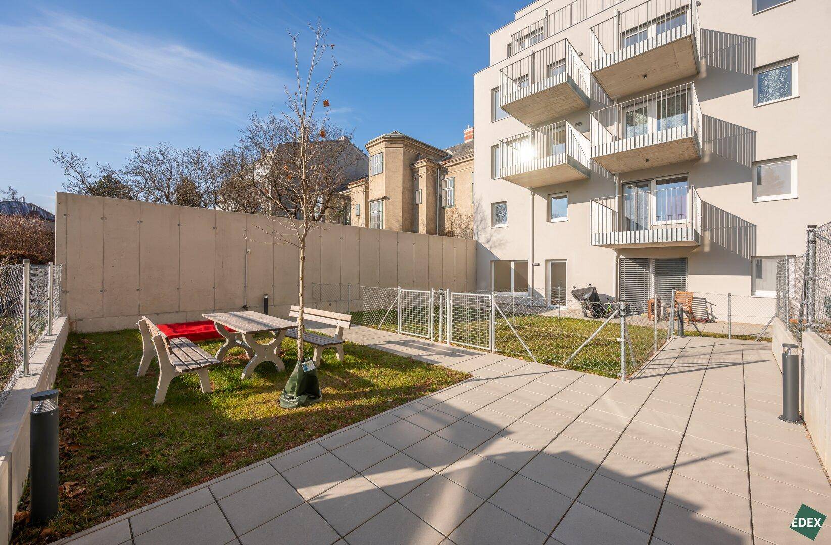 Gemeinschaftsgarten mit Sitzgelegenheiten und Rasenfläche, umgeben von moderner Architektur.