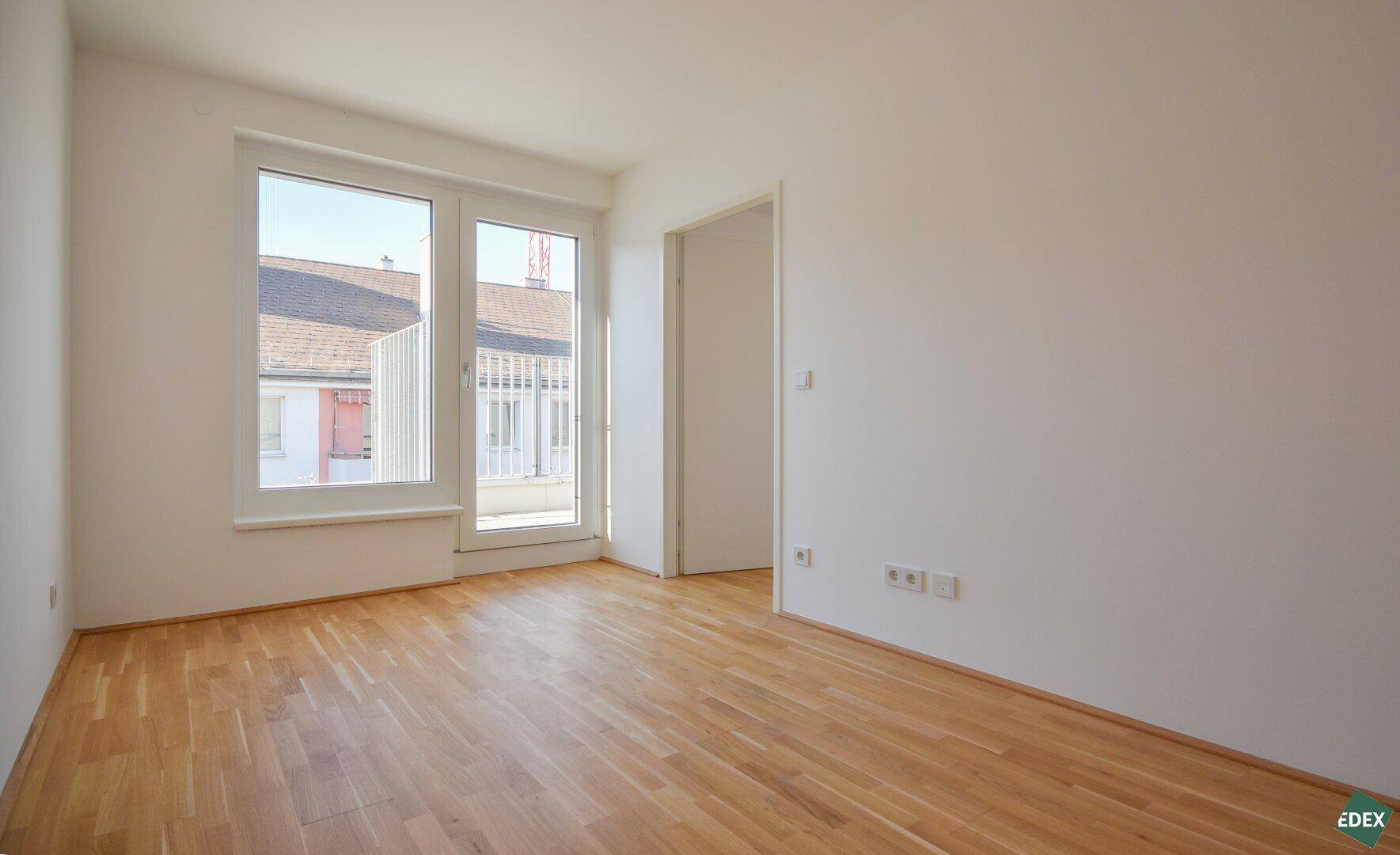 Geräumiges, helles Zimmer mit Parkettboden und Zugang zu einem Außenbereich.