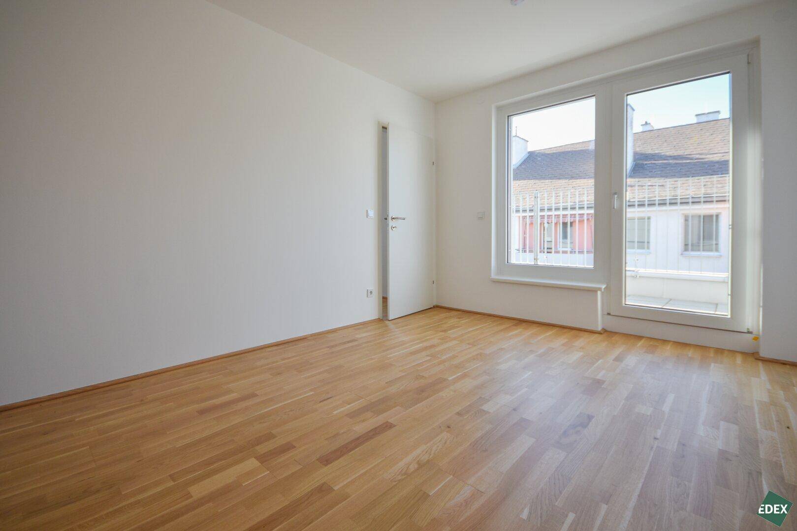 Helles Zimmer mit Holzboden und großen Fenstern, die einen Blick nach draußen ermöglichen.