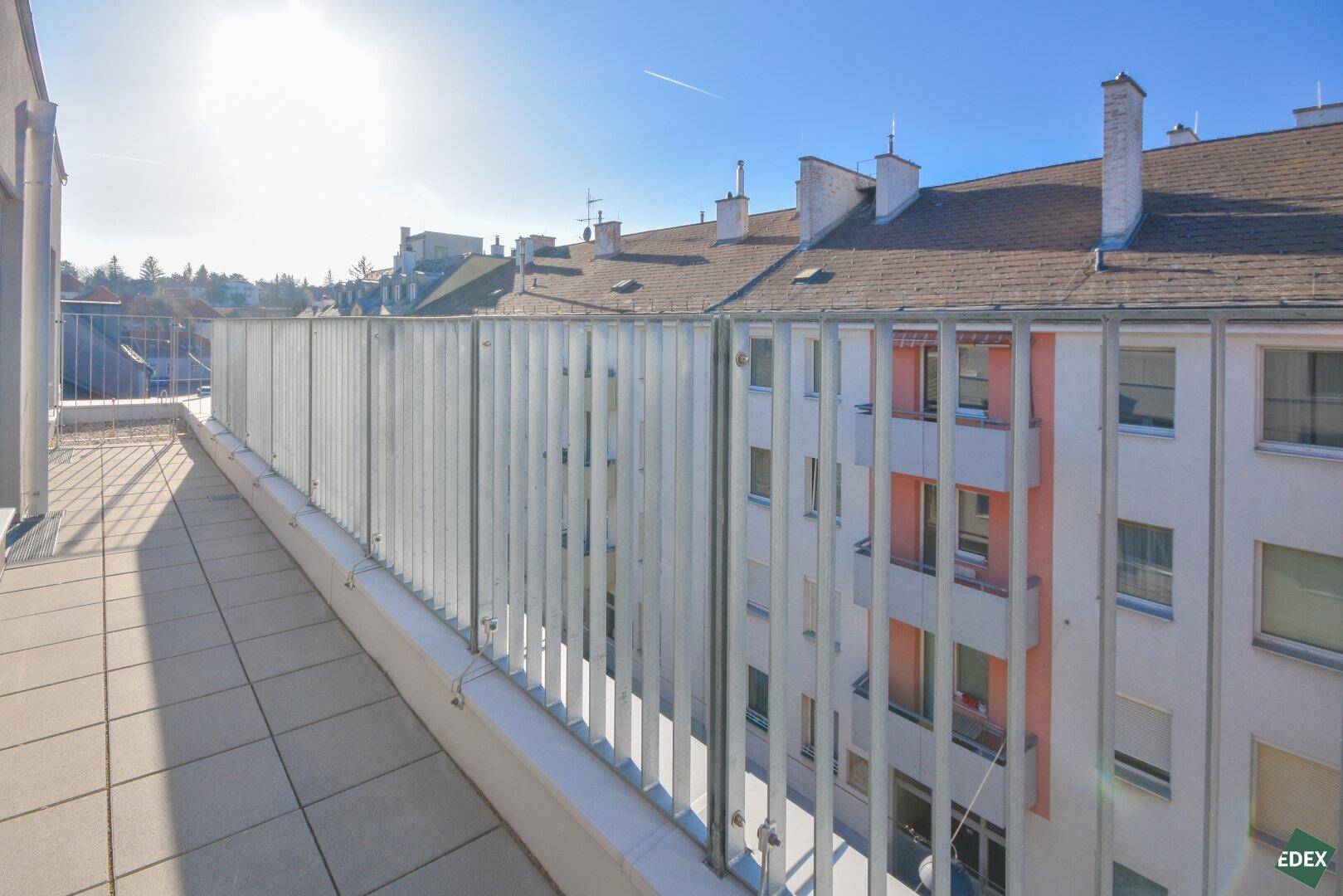 Sonniger Balkon mit Fliesenboden und Blick auf die umliegenden Gebäude und Dächer.