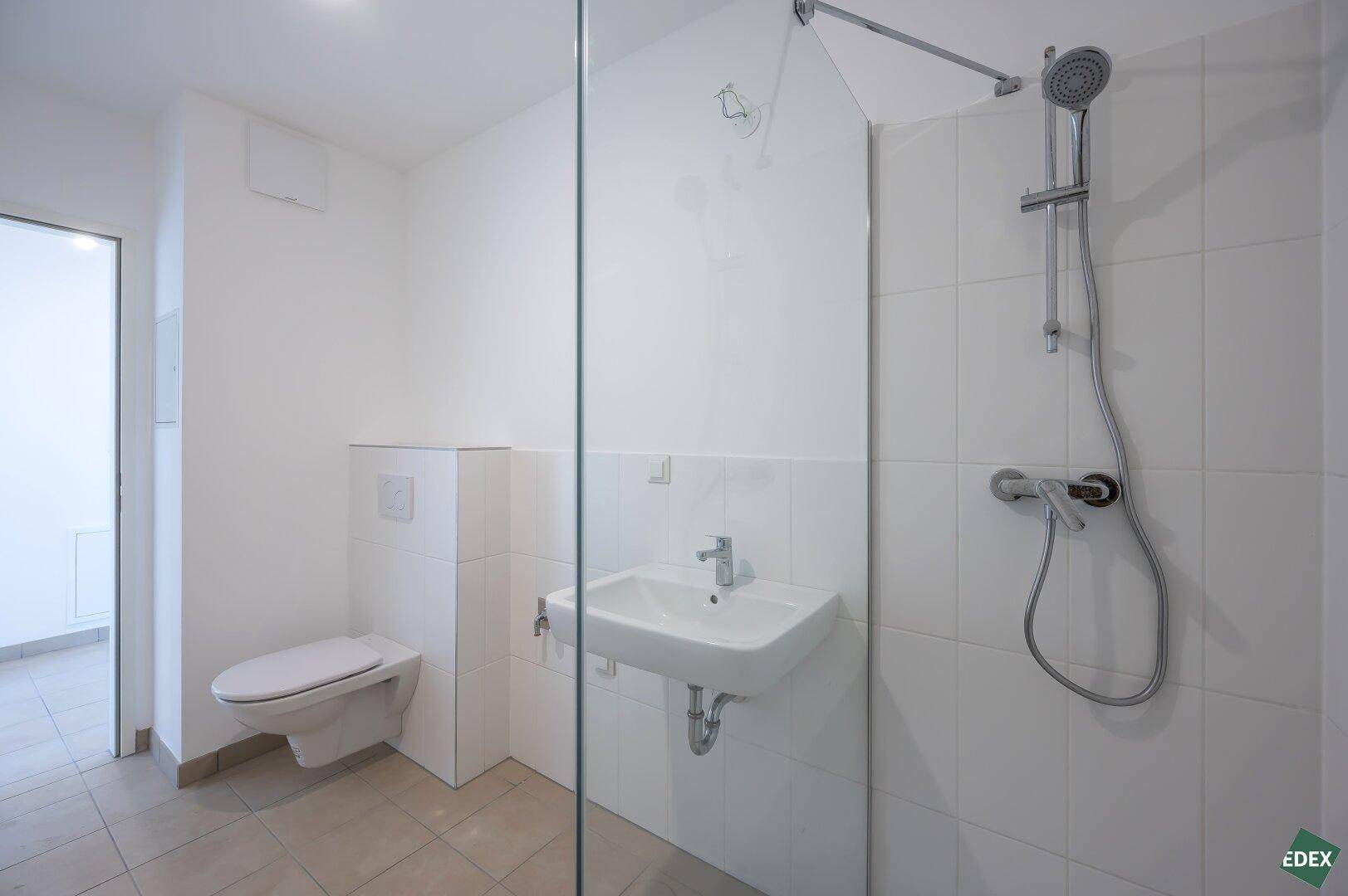 Helles Badezimmer mit moderner Duschkabine, Wand-WC und Waschbecken.