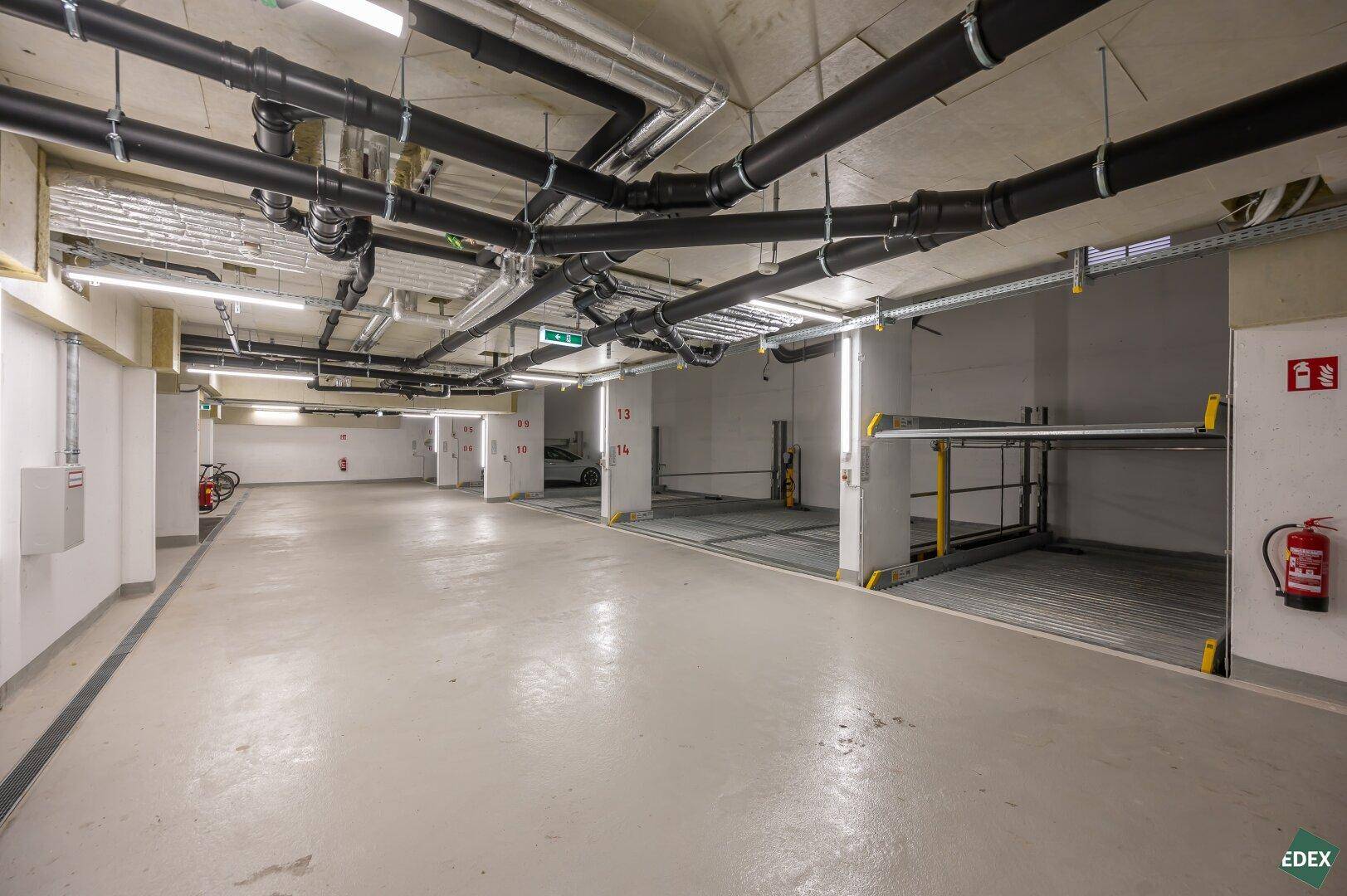 Tiefgarage mit automatischen Parksystemen und sichtbaren Rohrleitungen an der Decke.