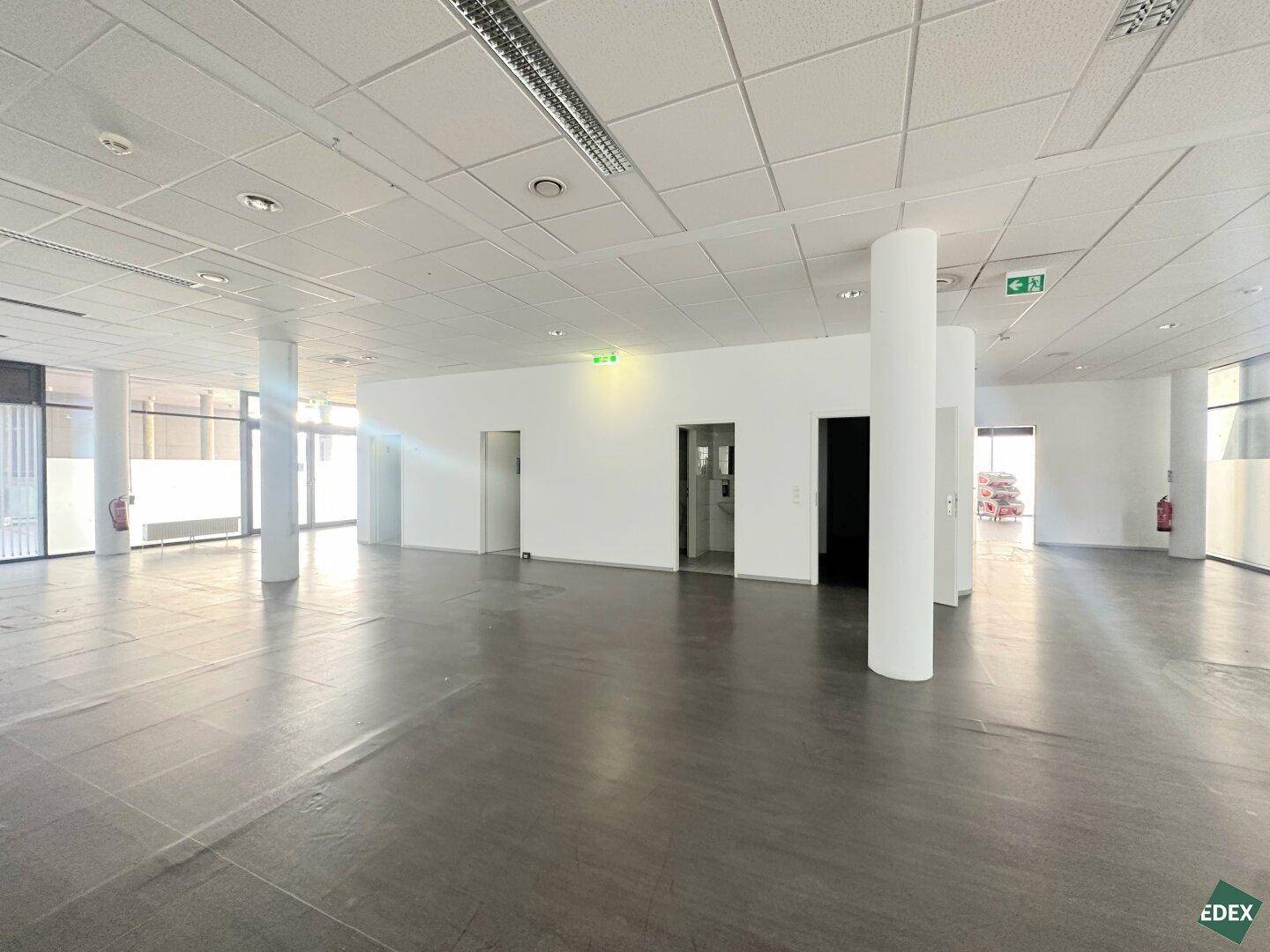Heller, leerer Gewerberaum mit weißen Wänden, Säulen und mehreren Türen, ideal für flexible Gestaltung.