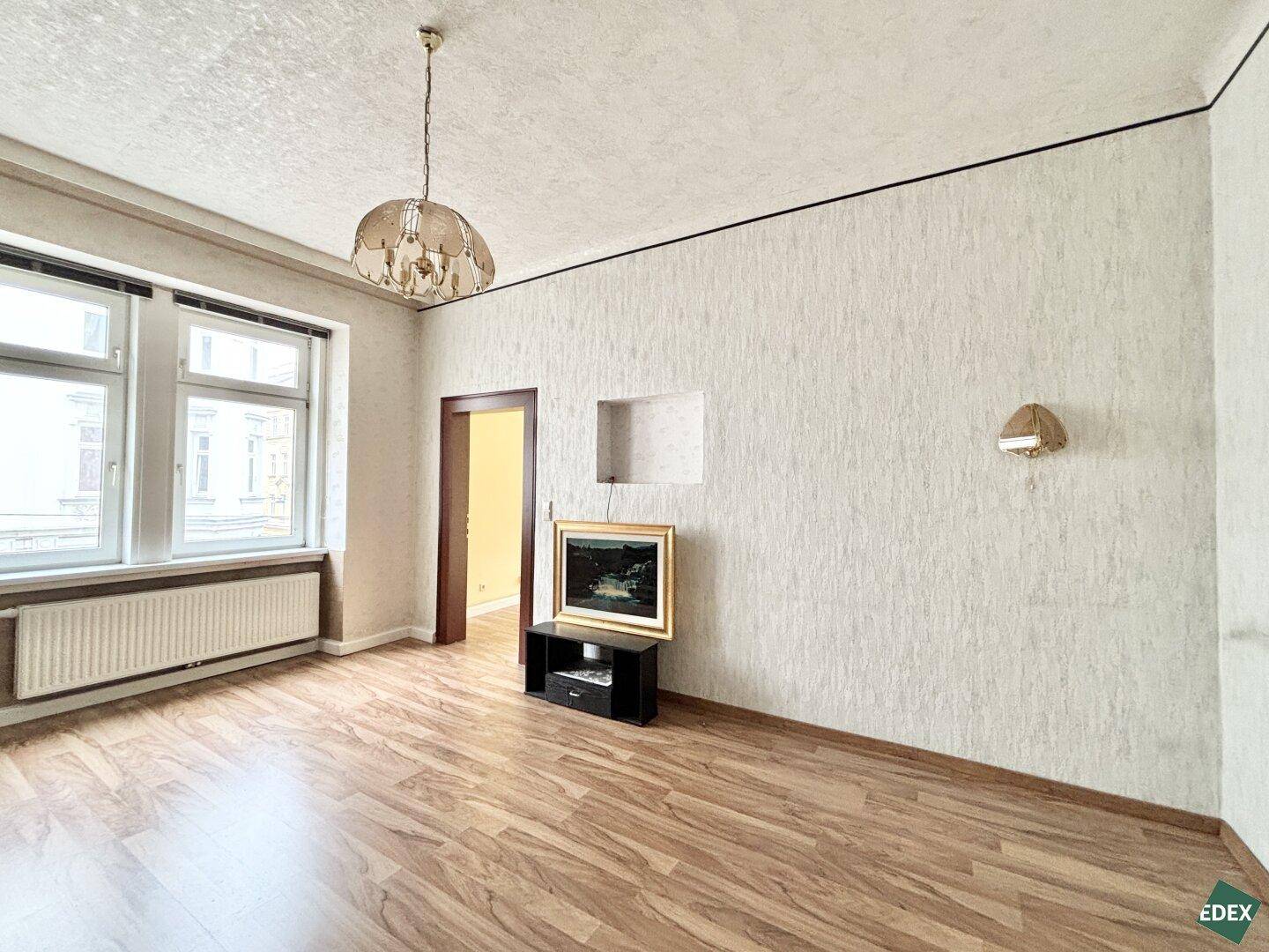 Wohnzimmer mit strukturierten Wänden, Laminatboden und klassischem Kronleuchter.