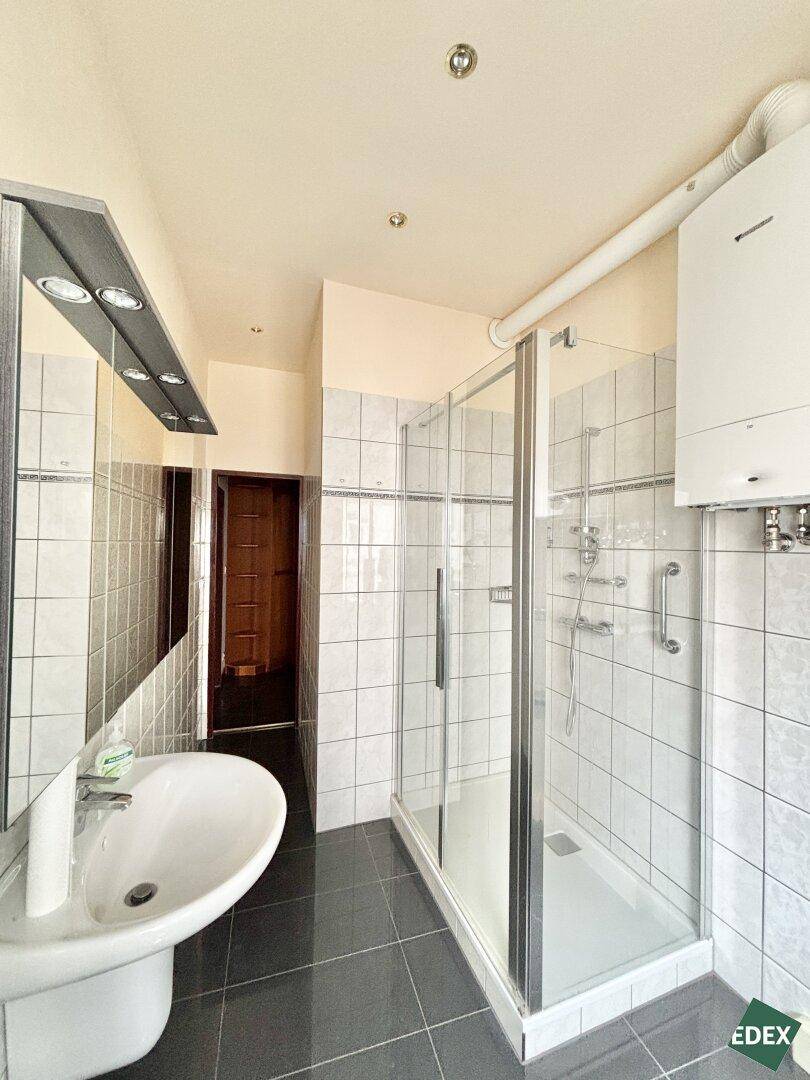 Funktionales Badezimmer mit Duschkabine, Waschbecken und Wandspiegel, ausgestattet mit Haltegriffen.