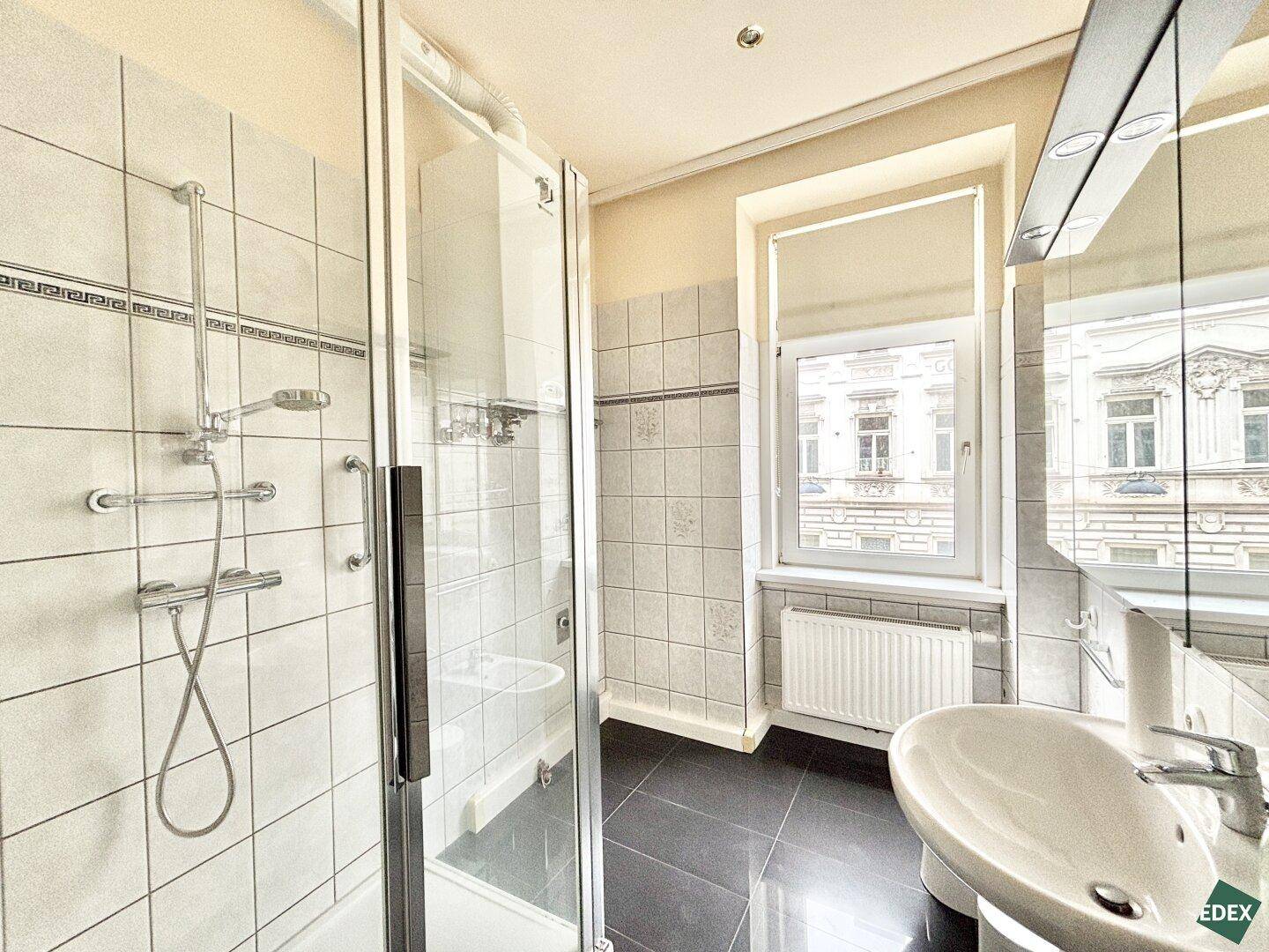 Badezimmer mit Duschkabine, Waschbecken, Spiegelschrank und Fenster für Tageslicht.