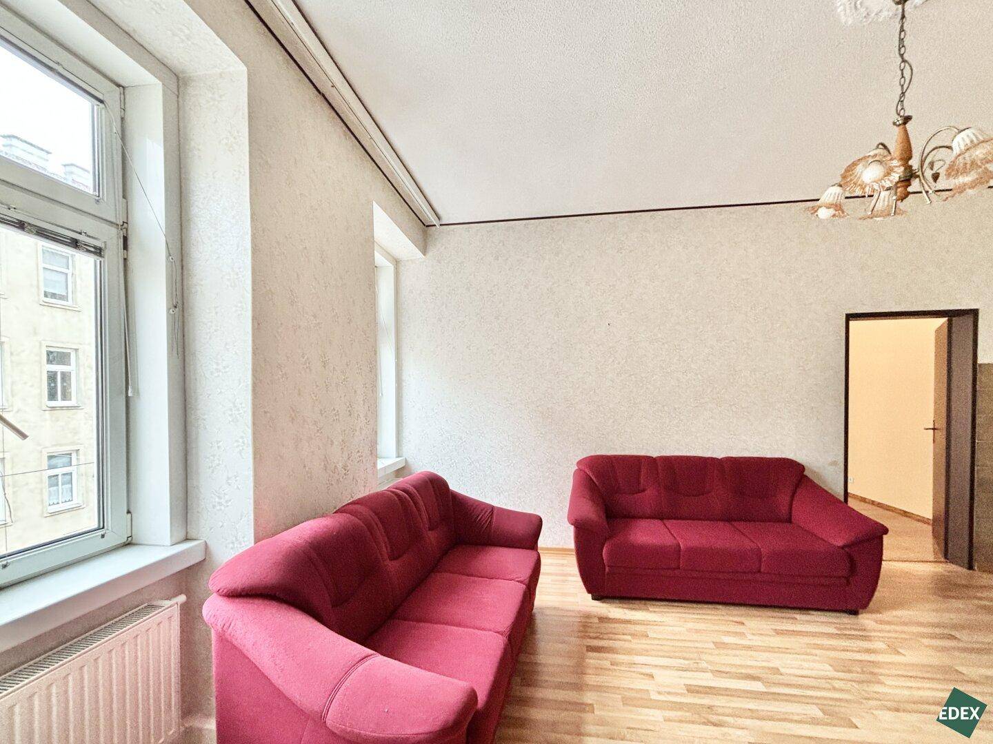 Wohnzimmer mit zwei roten Sofas, Laminatboden und großen Fenstern.