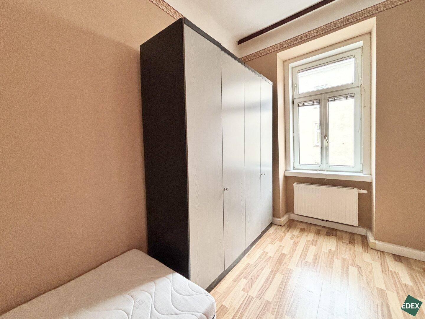 Schlafzimmer mit Einzelbett, großem Kleiderschrank und Laminatboden.