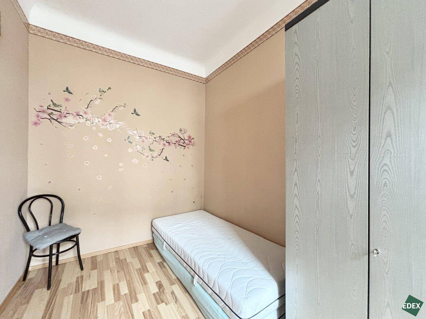 Kinderzimmer mit Einzelbett, kleinem Schrank und dekorativer Wandgestaltung.
