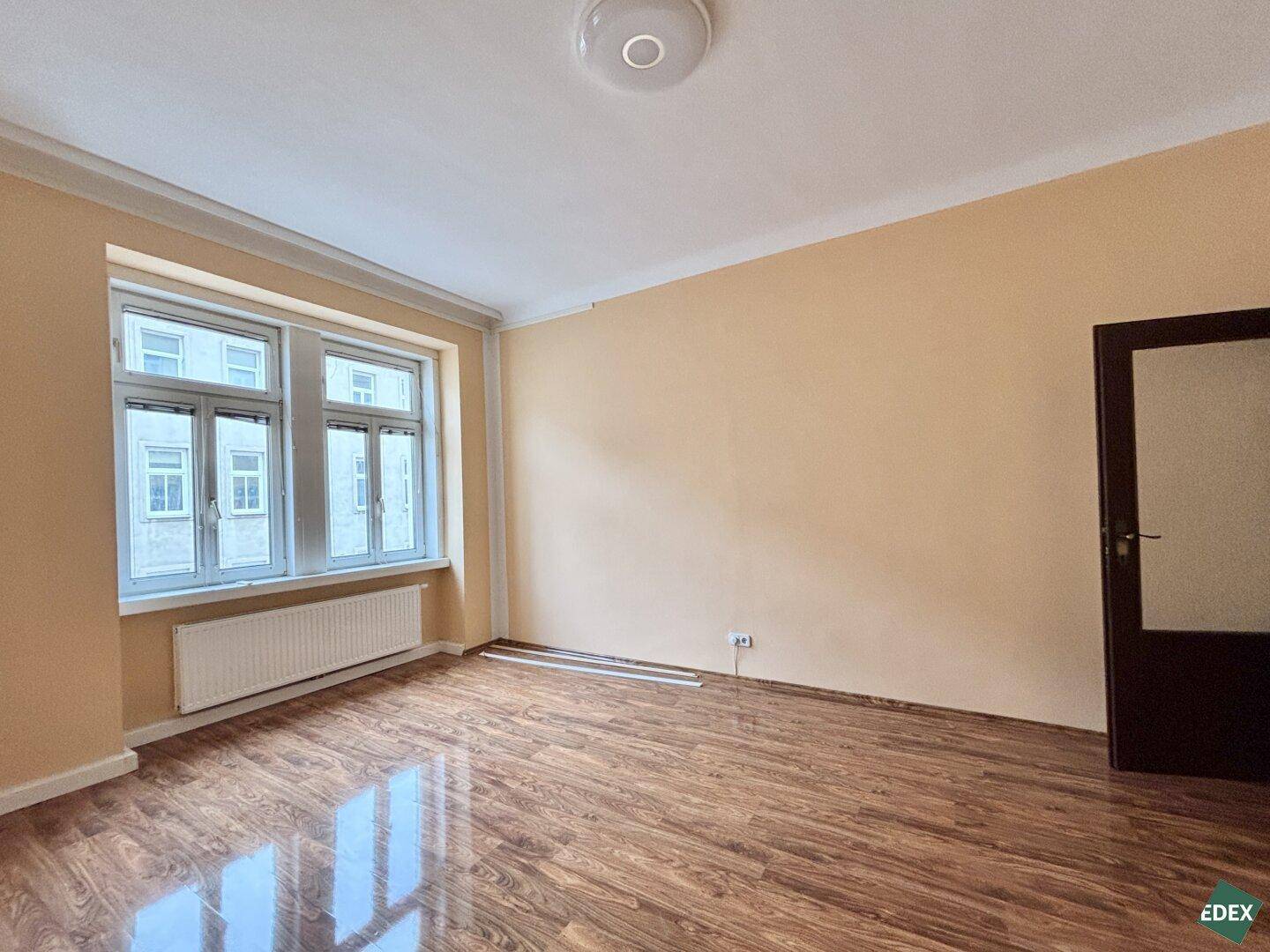 Heller, leerer Raum mit Laminatboden, hellen Wänden und zwei Fenstern.
