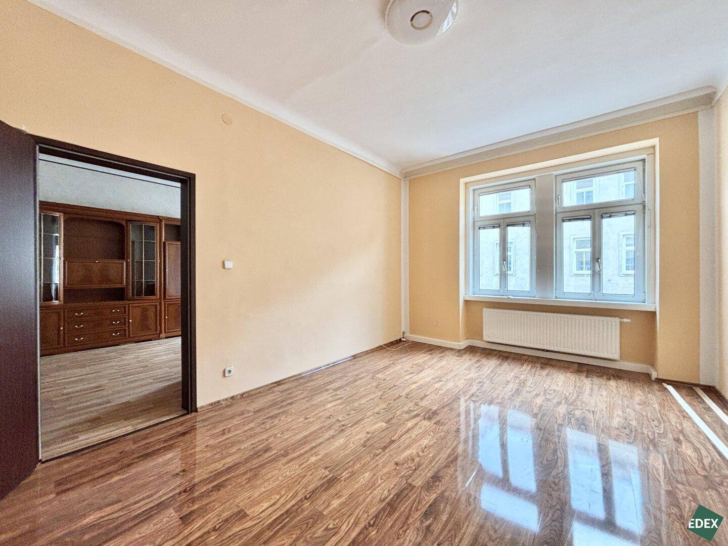 Geräumiger Raum mit Laminatboden und Zugang zu einem weiteren Zimmer mit Holzmöbeln.