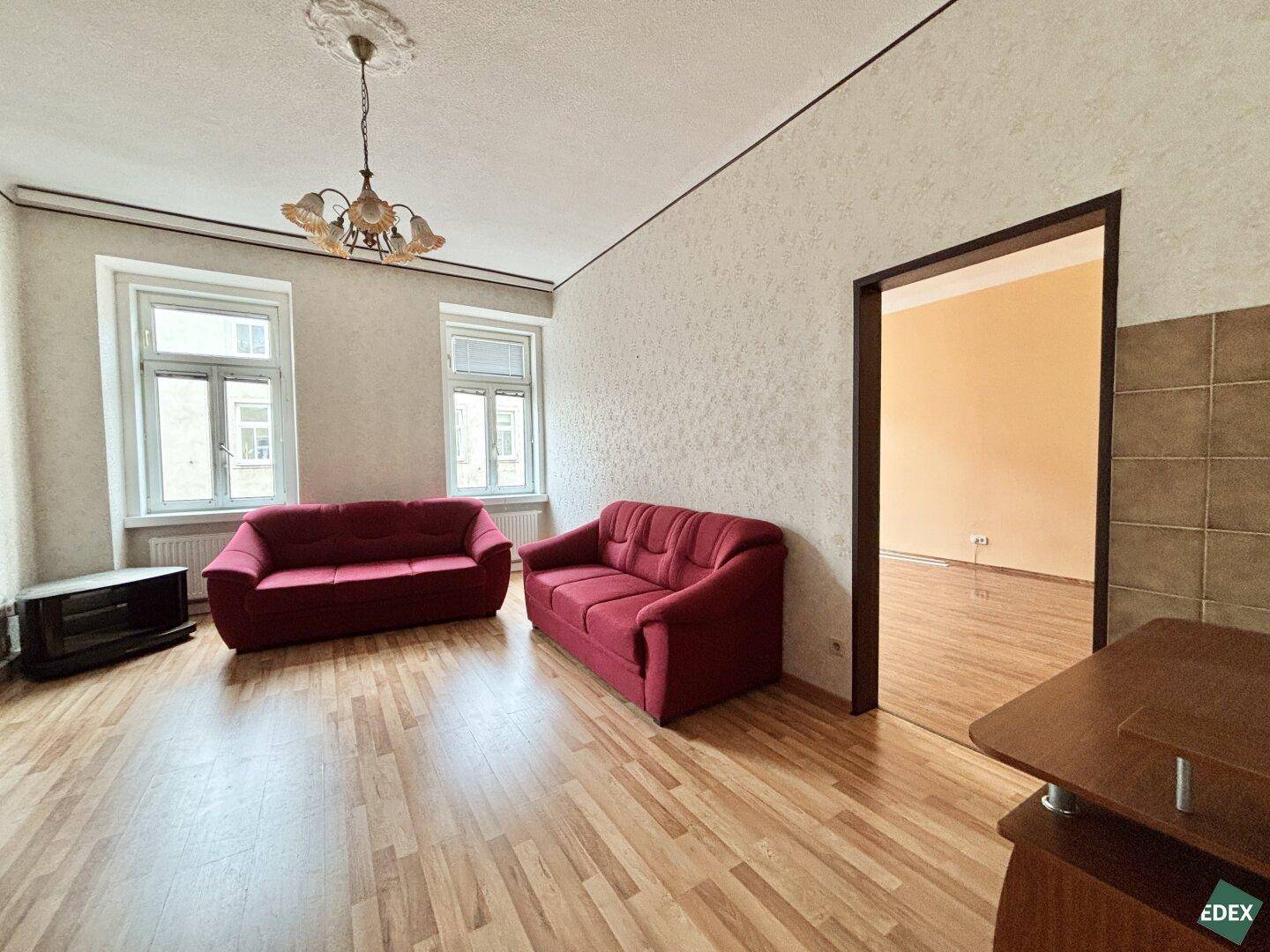Wohnzimmer mit roten Sofas, Laminatboden und Blick aus den Fenstern.