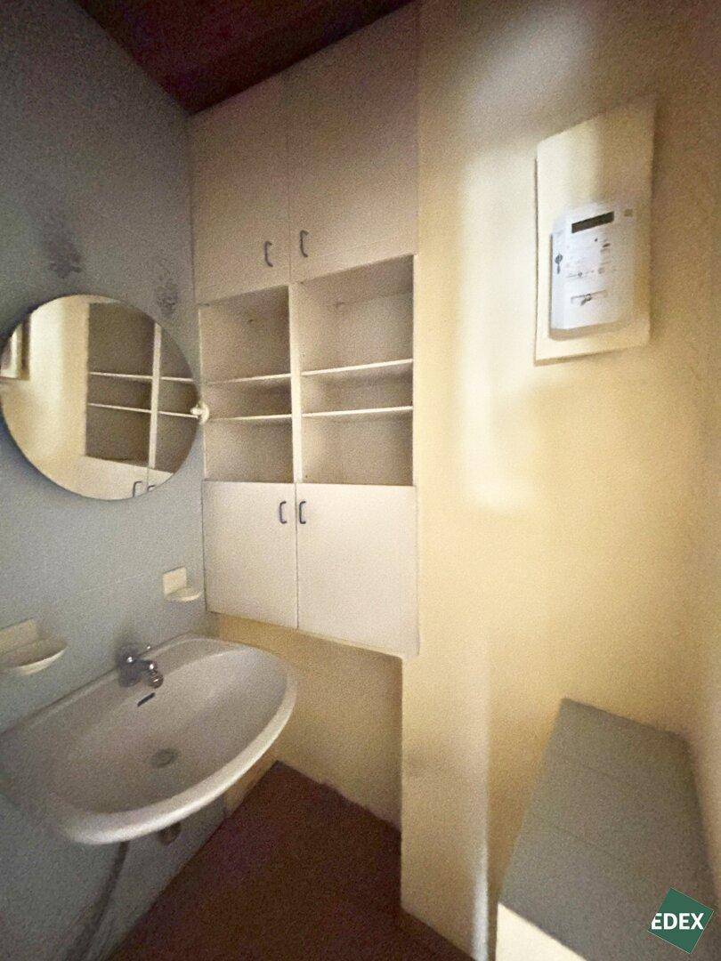 Badezimmer mit Waschbecken, Spiegelschrank und Ablageflächen, in einfachem Zustand.