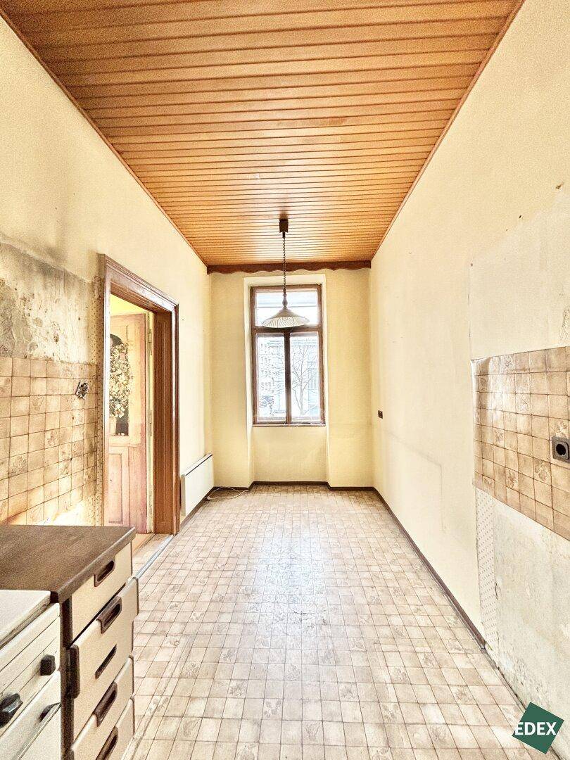 Lange Küche mit Holzdecke, gefliesten Wänden und einem Fenster zur Hofseite.