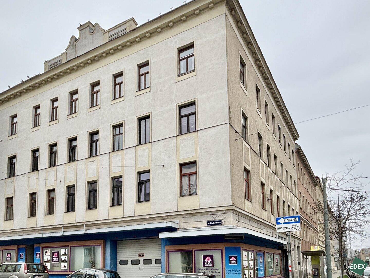 Eckgebäude eines Altbaus mit mehreren Etagen und Geschäften im Erdgeschoss.