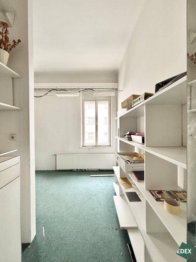 Leerer Büroraum mit Regalen, grünem Teppichboden und Fenster.