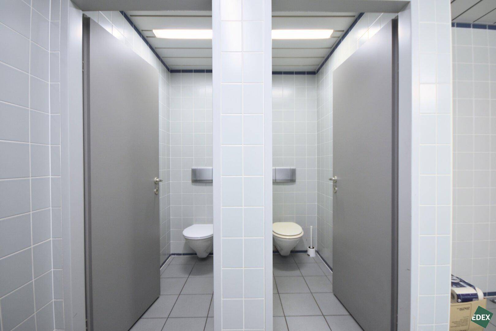 Zwei separate Toilettenkabinen in einem gefliesten Waschraum mit hellen Fliesen.