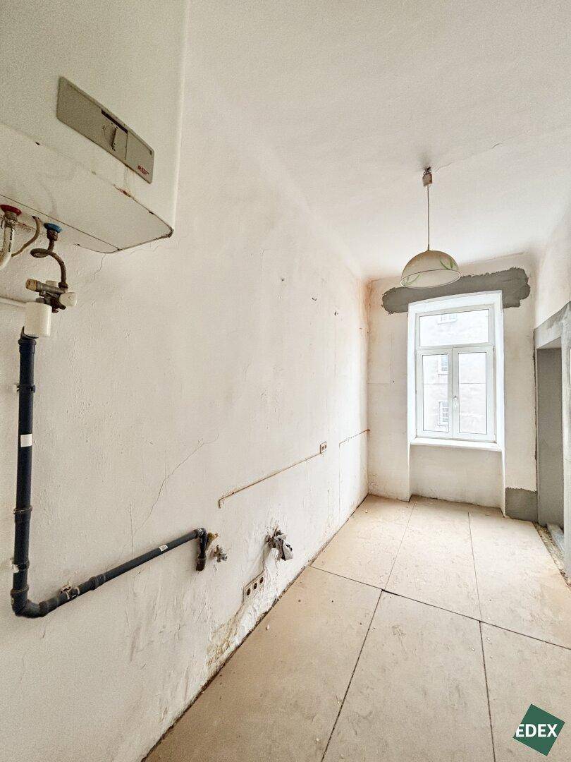 Funktionsraum mit Fliesenboden, sichtbaren Rohren und einem Warmwasserbereiter an der Wand, bereit für die Nutzung.