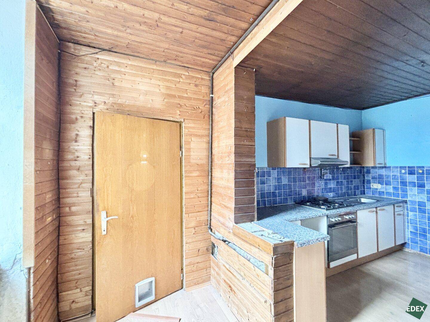 Einfache Küche mit blauen Fliesen und Holzdecke, bereit für eine Modernisierung.