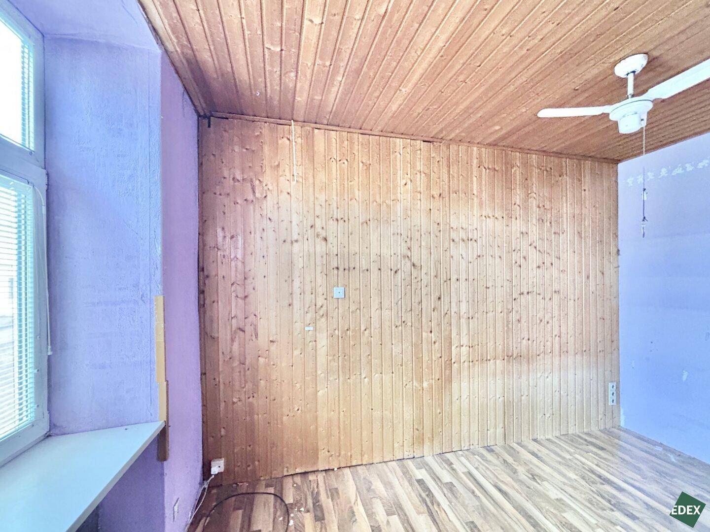 Raum mit Holzvertäfelung und Deckenventilator, der auf eine Renovierung wartet.