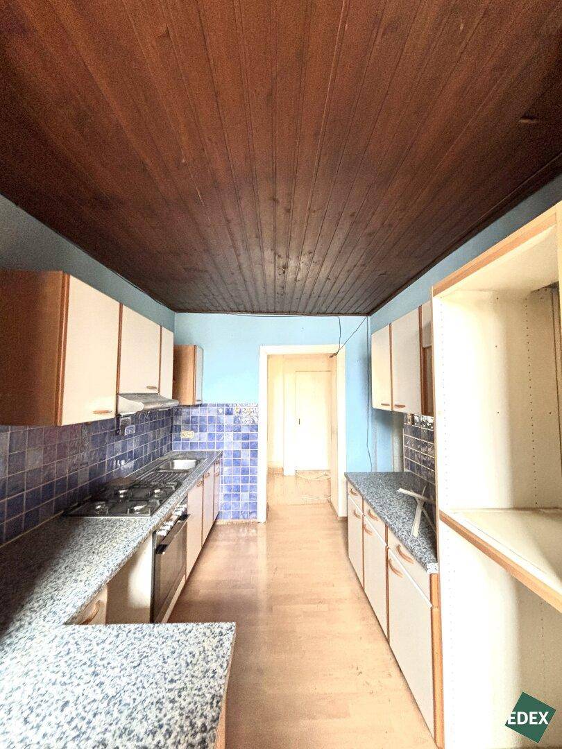 Schmale Küche mit blauen Fliesen und Holzdecke, die eine Modernisierung benötigt.