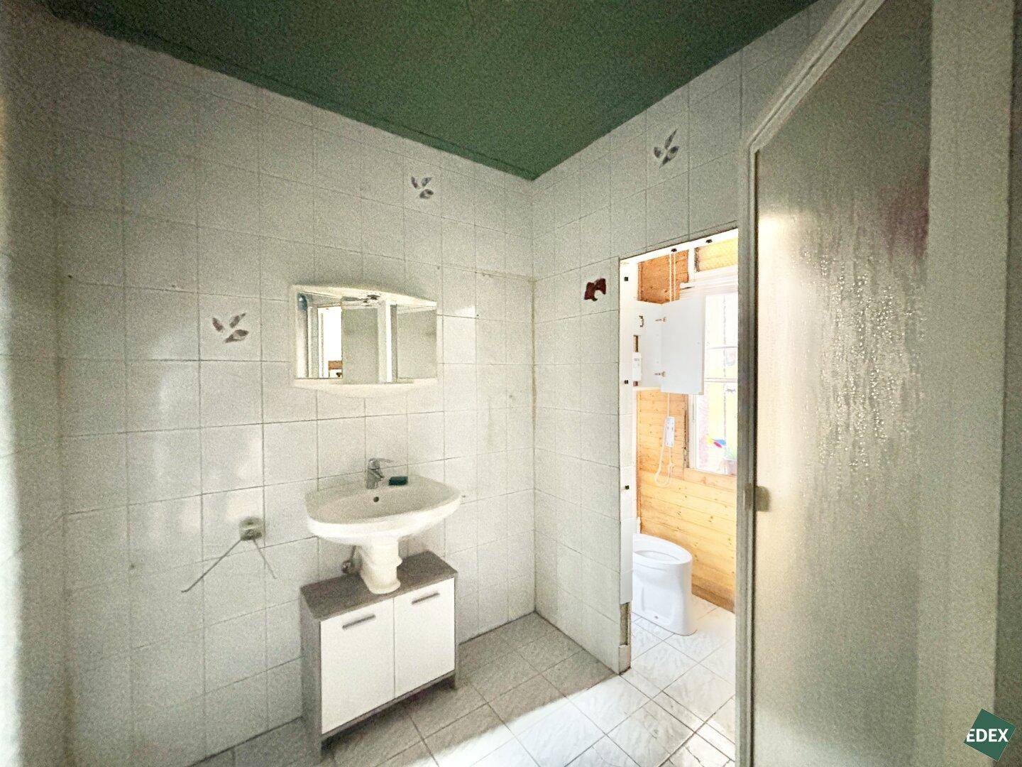 Gefliestes Badezimmer mit Waschbecken und Spiegelschrank, angrenzend an eine Toilette.