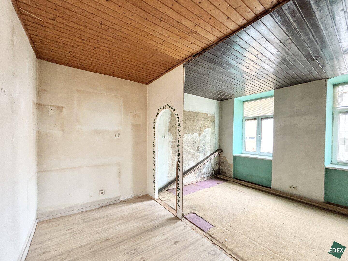 Renovierungsbedürftiger Raum mit Holzbalkendecke und teilweise entfernten Wänden.