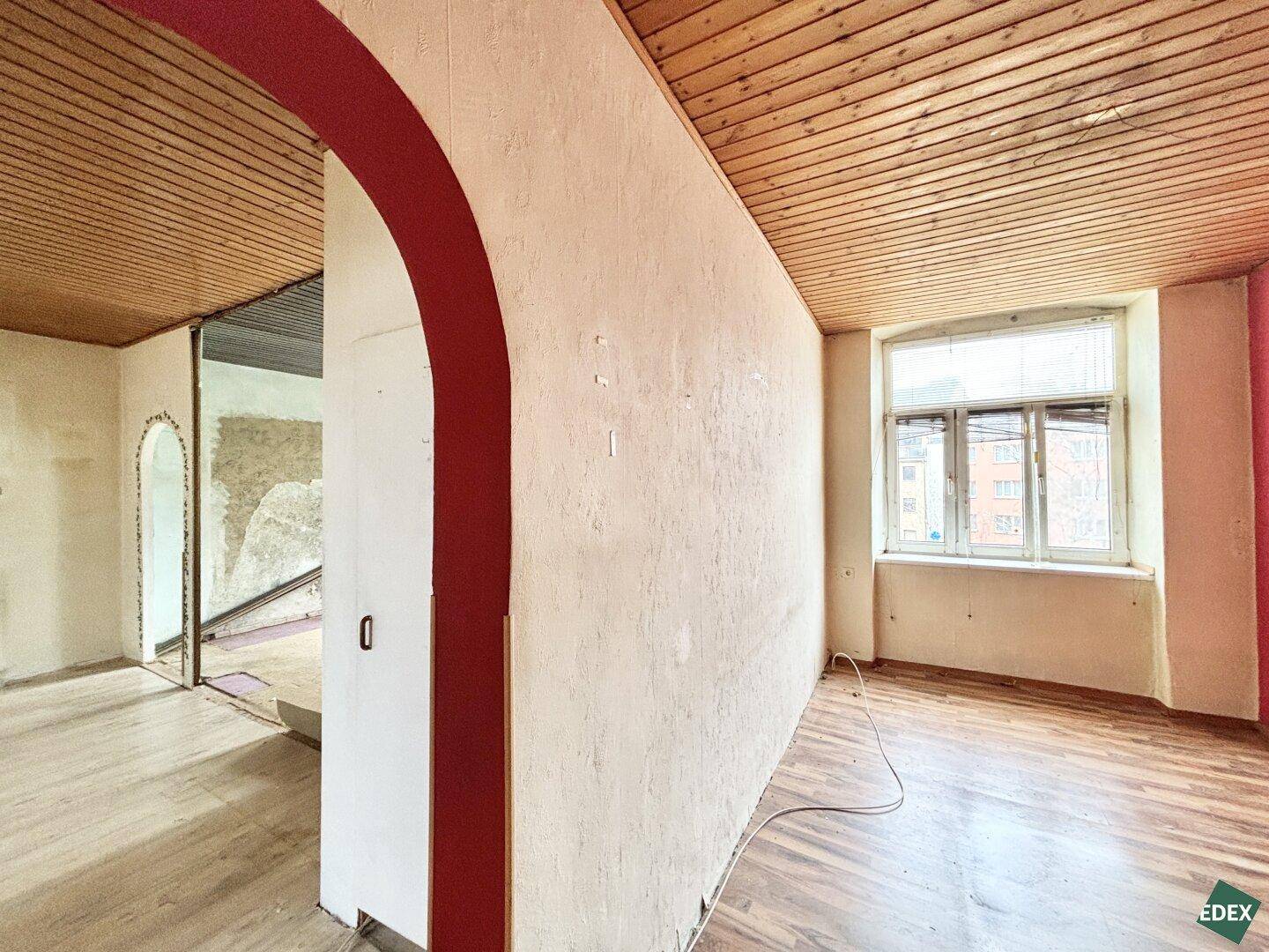 Renovierungsbedürftiger Raum mit Holzbalkendecke und rotem Bogen, bereit zur Neugestaltung.