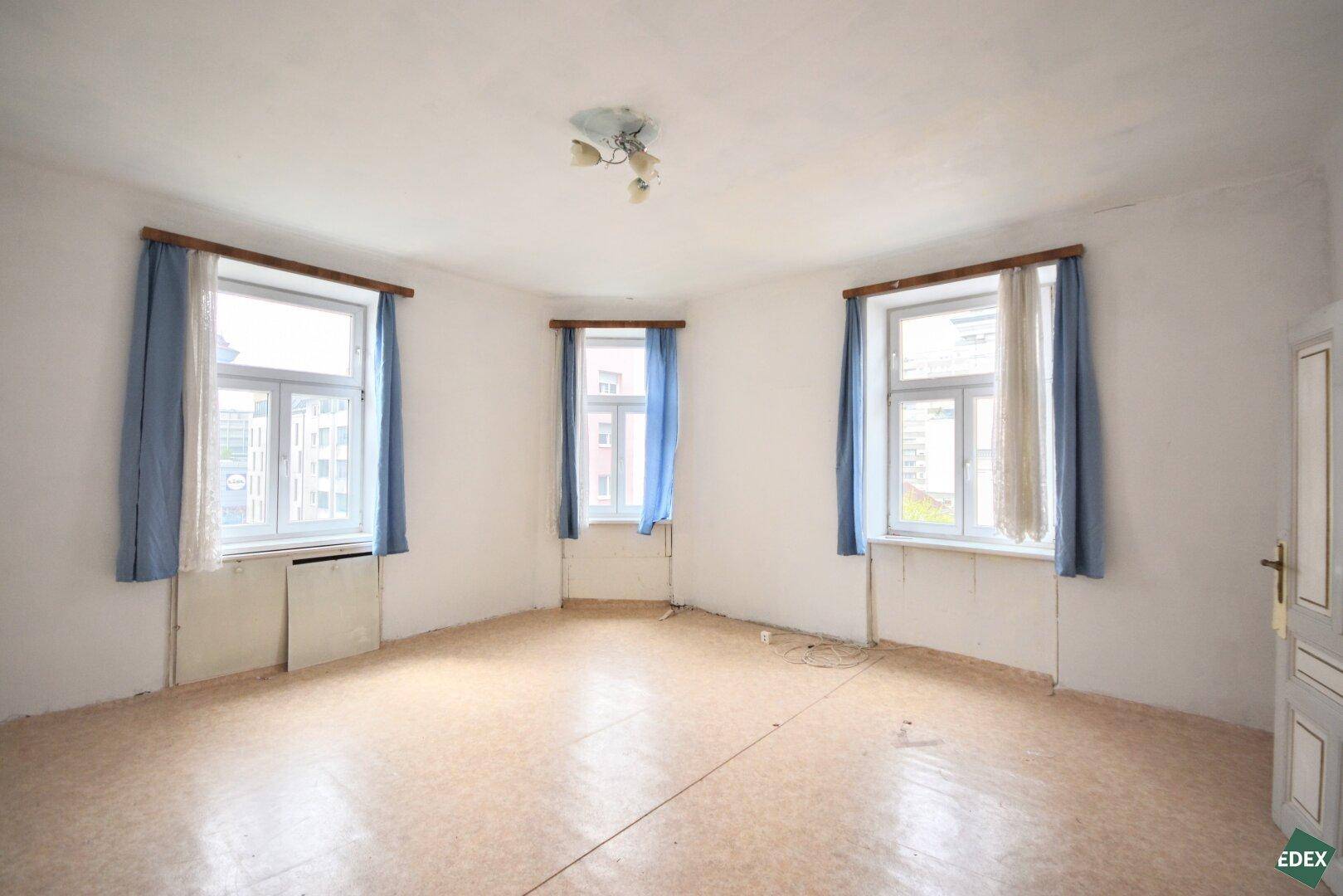 Helles Zimmer mit drei Fenstern, Linoleumboden und einfacher Ausstattung, ideal für eine Renovierung.