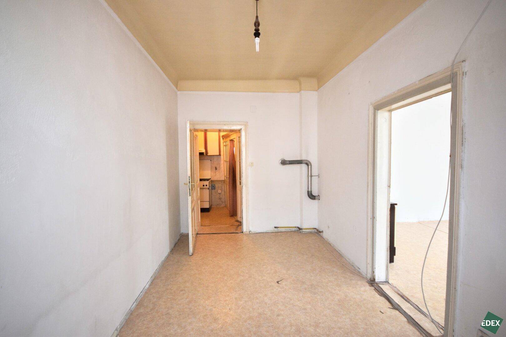 Leeres Zimmer mit Linoleumboden und zwei Türen, die zu anderen Bereichen der Wohnung führen.