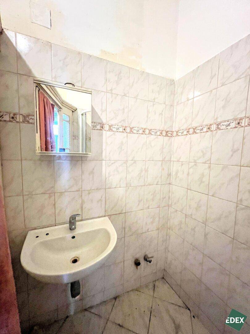 Kleines Badezimmer mit Waschbecken und Wandfliesen, das eine Modernisierung benötigt.