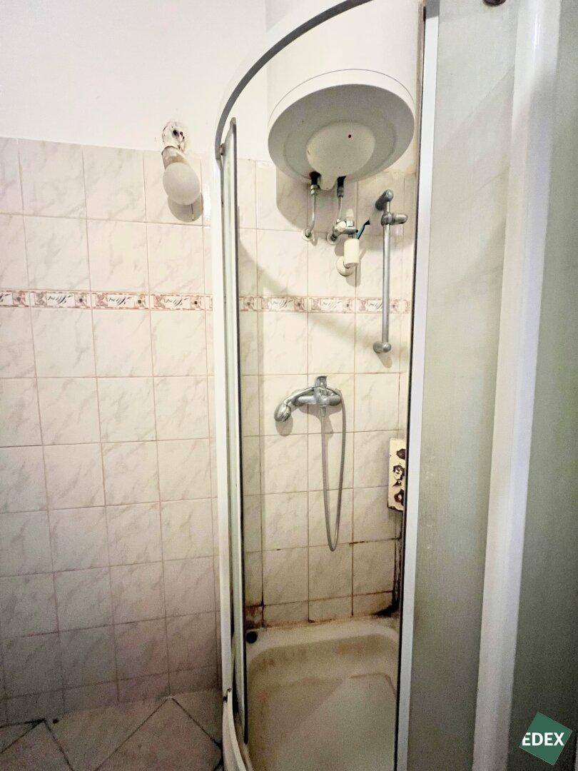 Duschkabine mit Boiler und einfachen Fliesen, die den Bedarf an Renovierung zeigt.