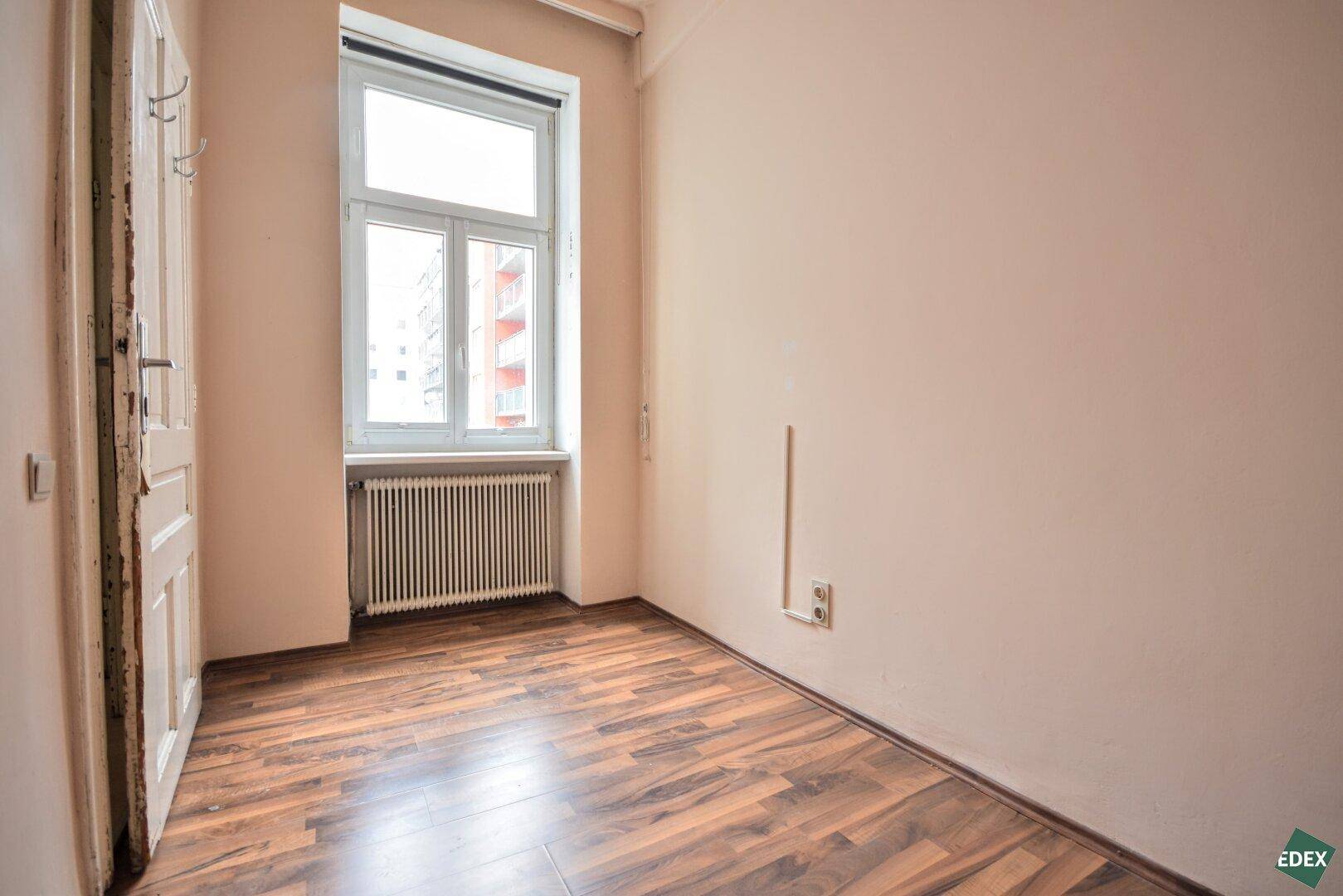 Kleines, helles Zimmer mit Laminatboden, einem Fenster und einfacher Ausstattung.
