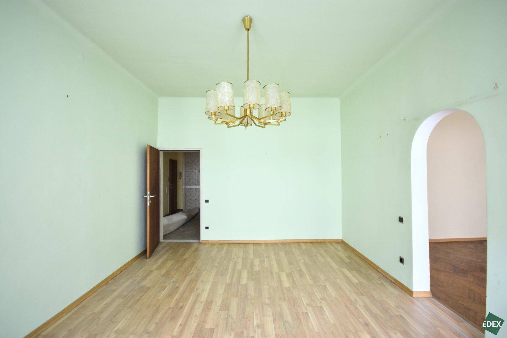 Geräumiges Zimmer mit hellgrünen Wänden, Parkettboden und Zugang zu weiteren Räumen.